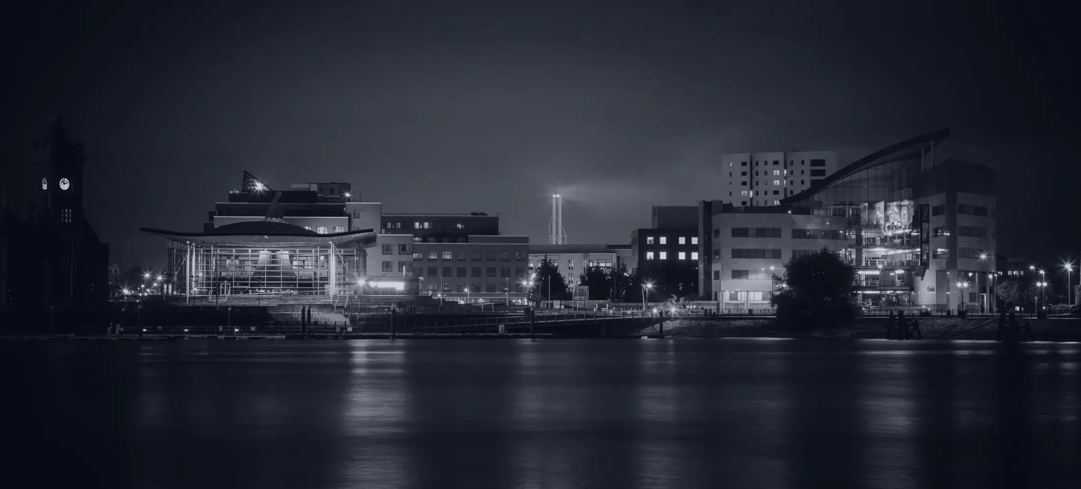Cardiff Bay at night, with the Senedd, the Welsh Parliament building, lit up on the waterfront.