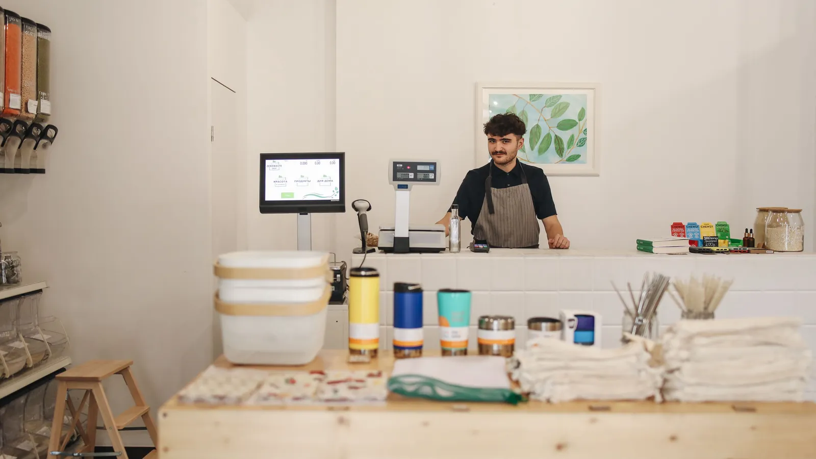 A shop owner standing behind the counter of a small refill shop